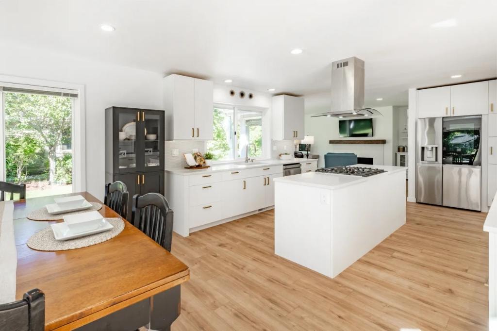Open-concept kitchen with white cabinets, gold hardware, and wood dining table