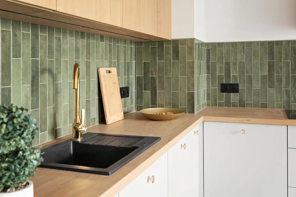 Kitchen with green tile backsplash, natural wood cabinetry, and brass fixtures