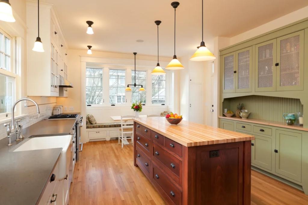 Traditional kitchen with sage green cabinets, butcher block island, and pendant lights